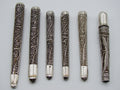 Six antique silver filigree mouthpieces arranged side by side, showing scrolling wire decoration and smooth ends