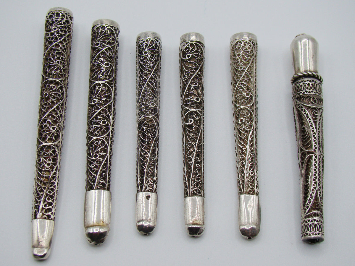 Six antique silver filigree mouthpieces arranged side by side, showing scrolling wire decoration and smooth ends