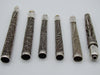 Horizontal reverse arrangement of six silver mouthpieces showing scrolling wirework and surface patina