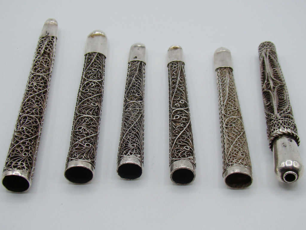 Horizontal reverse arrangement of six silver mouthpieces showing scrolling wirework and surface patina