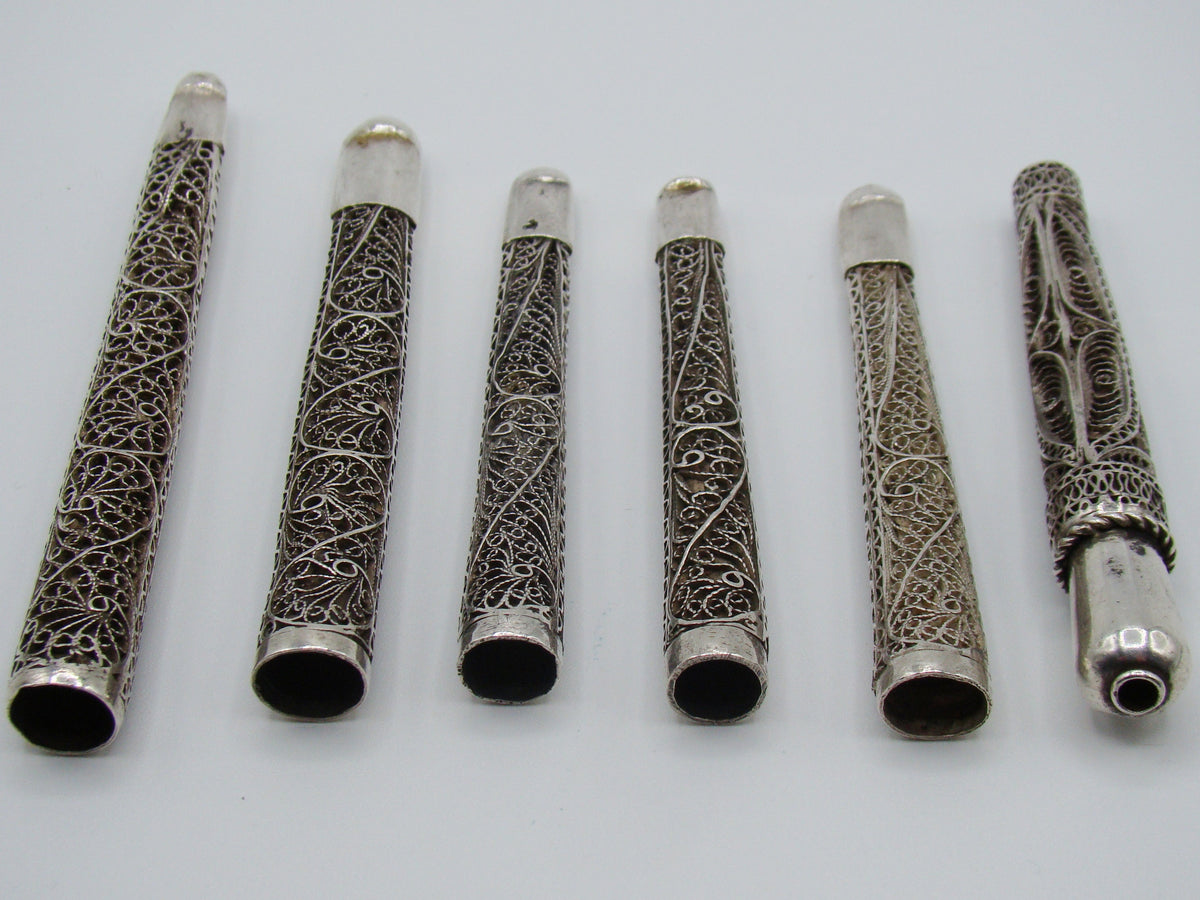 Horizontal reverse arrangement of six silver mouthpieces showing scrolling wirework and surface patina