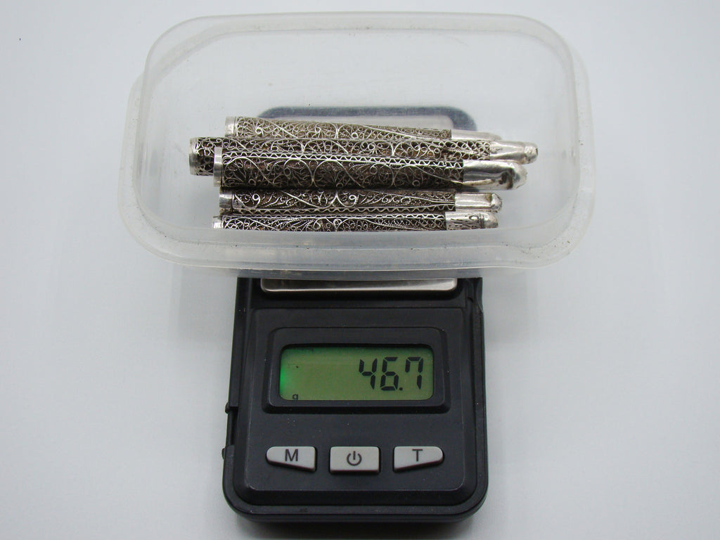 Six antique silver filigree mouthpieces in a tray on a digital scale displaying 46.7 grams