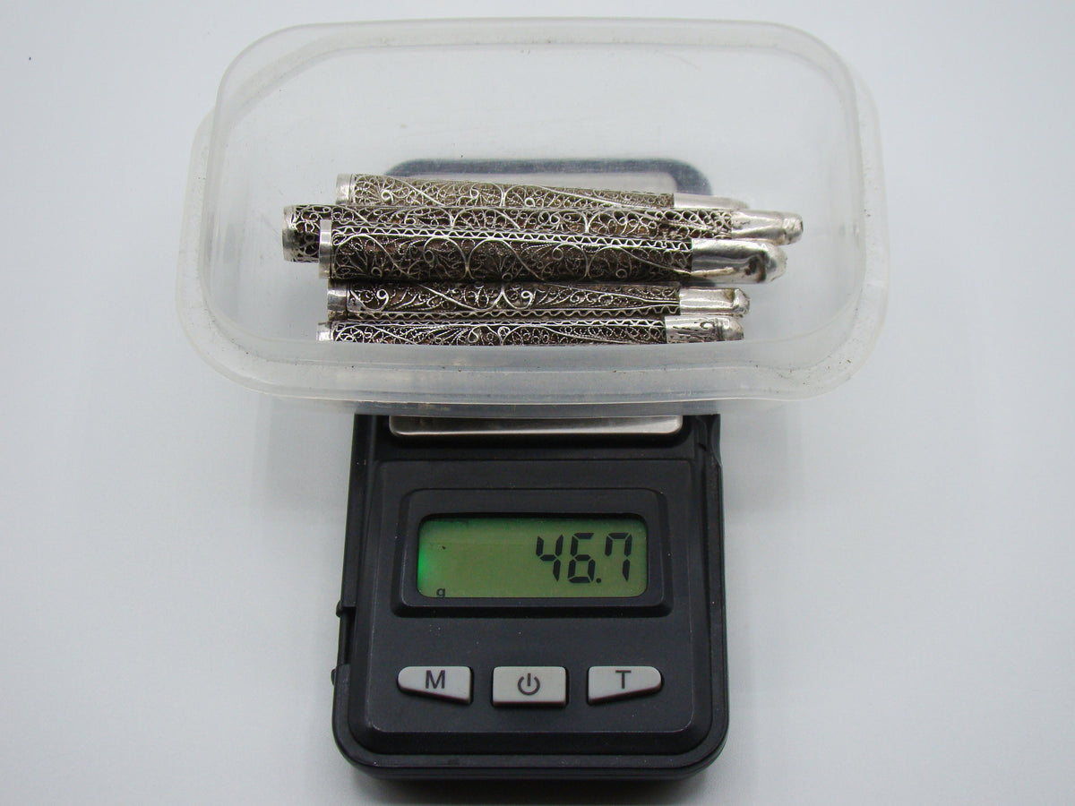Six antique silver filigree mouthpieces in a tray on a digital scale displaying 46.7 grams