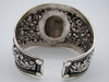 Angled front view of wide silver floral cuff with raised oval centrepiece and open back