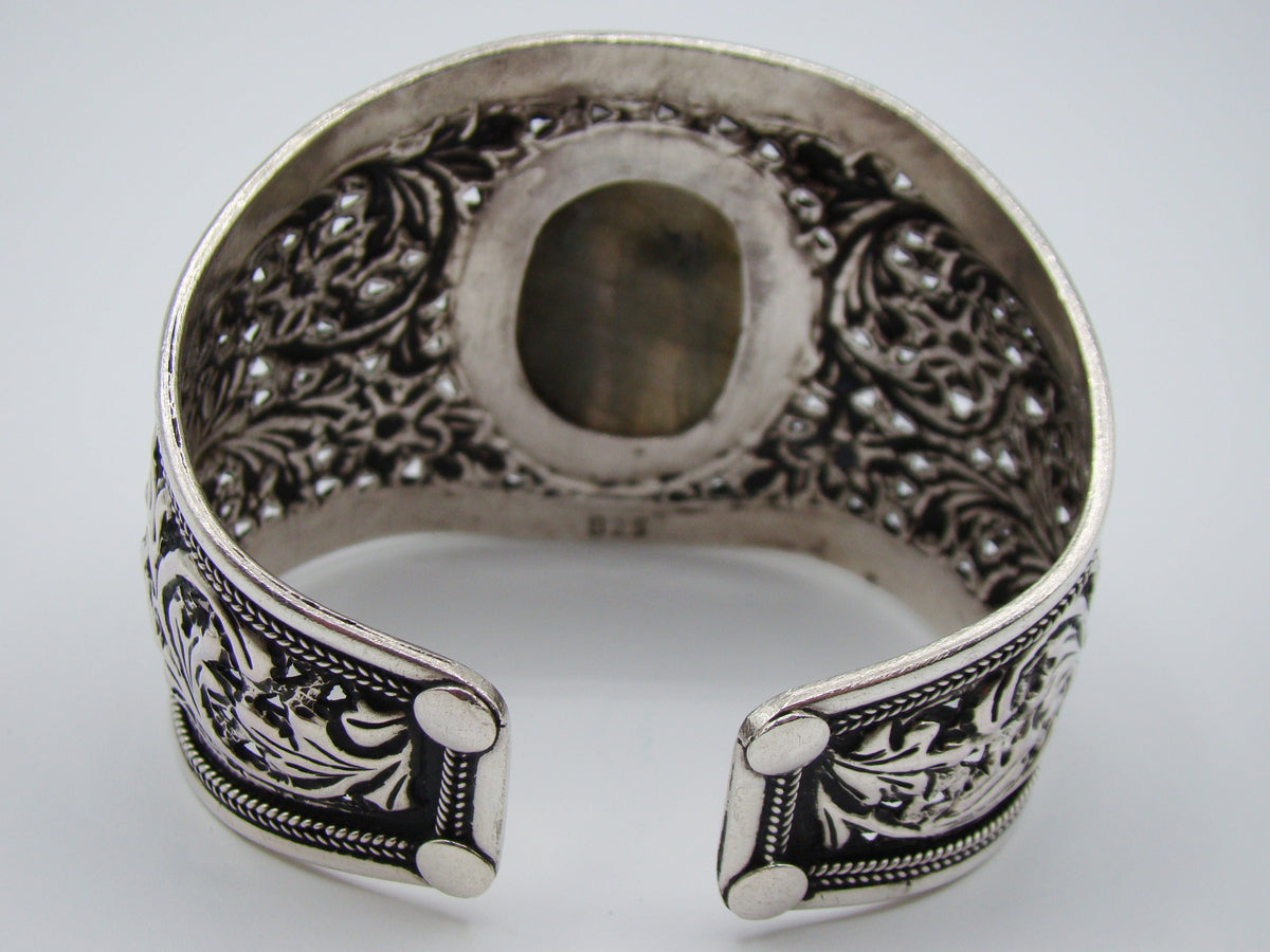 Angled front view of wide silver floral cuff with raised oval centrepiece and open back