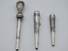 Three antique silver mouthpieces with engraved decoration and an ornate gold-coloured accent on the largest piece