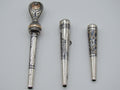 Three antique silver mouthpieces with engraved decoration and an ornate gold-coloured accent on the largest piece