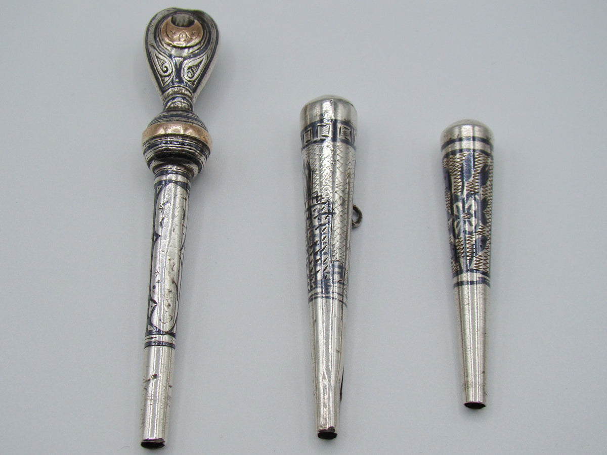 Three antique silver mouthpieces with engraved decoration and an ornate gold-coloured accent on the largest piece