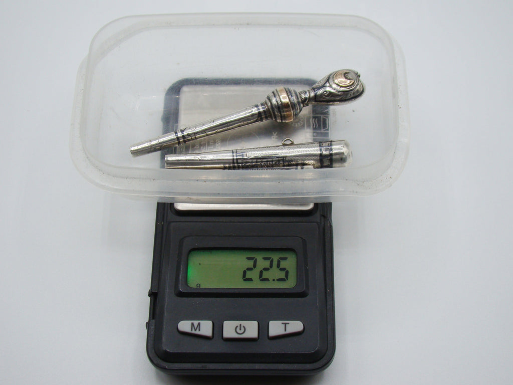 Three antique silver mouthpieces on a scale displaying 22.5 grams
