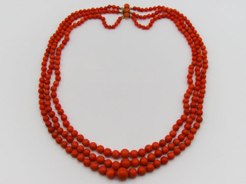 Three-strand red coral necklace with graduated beads and a clasp joining the strands at the back