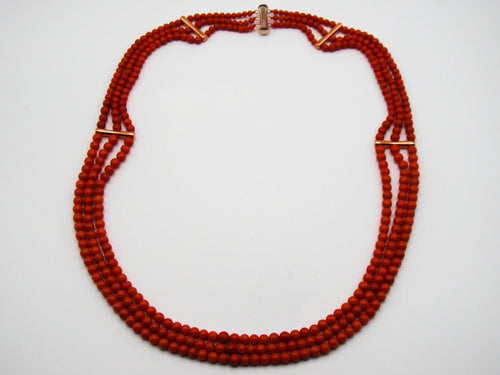 Three-strand red coral necklace with graduated beads and four spacer bars, laid flat on a white background